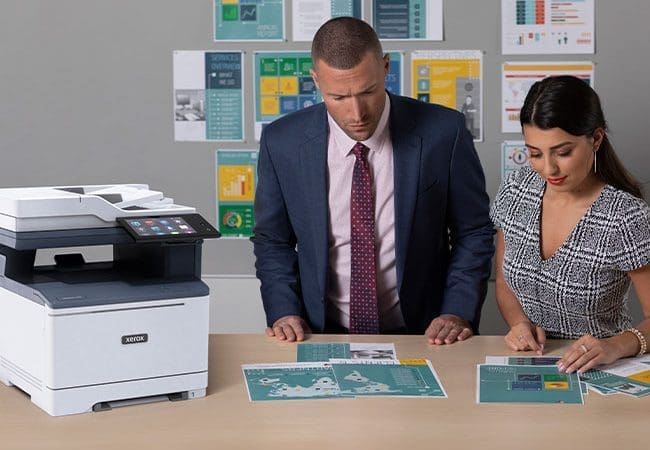 Deux personnes examinent des impressions couleur devant un multifonction Xerox VersaLink C415