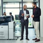 Deux hommes dans un bureau discutent sur une tablette à côté d'une imprimante multifonction couleur Xerox® AltaLink® série C8200 Deux hommes dans un bureau discutent sur une tablette à côté d'une imprimante multifonction couleur Xerox® AltaLink® série C8200