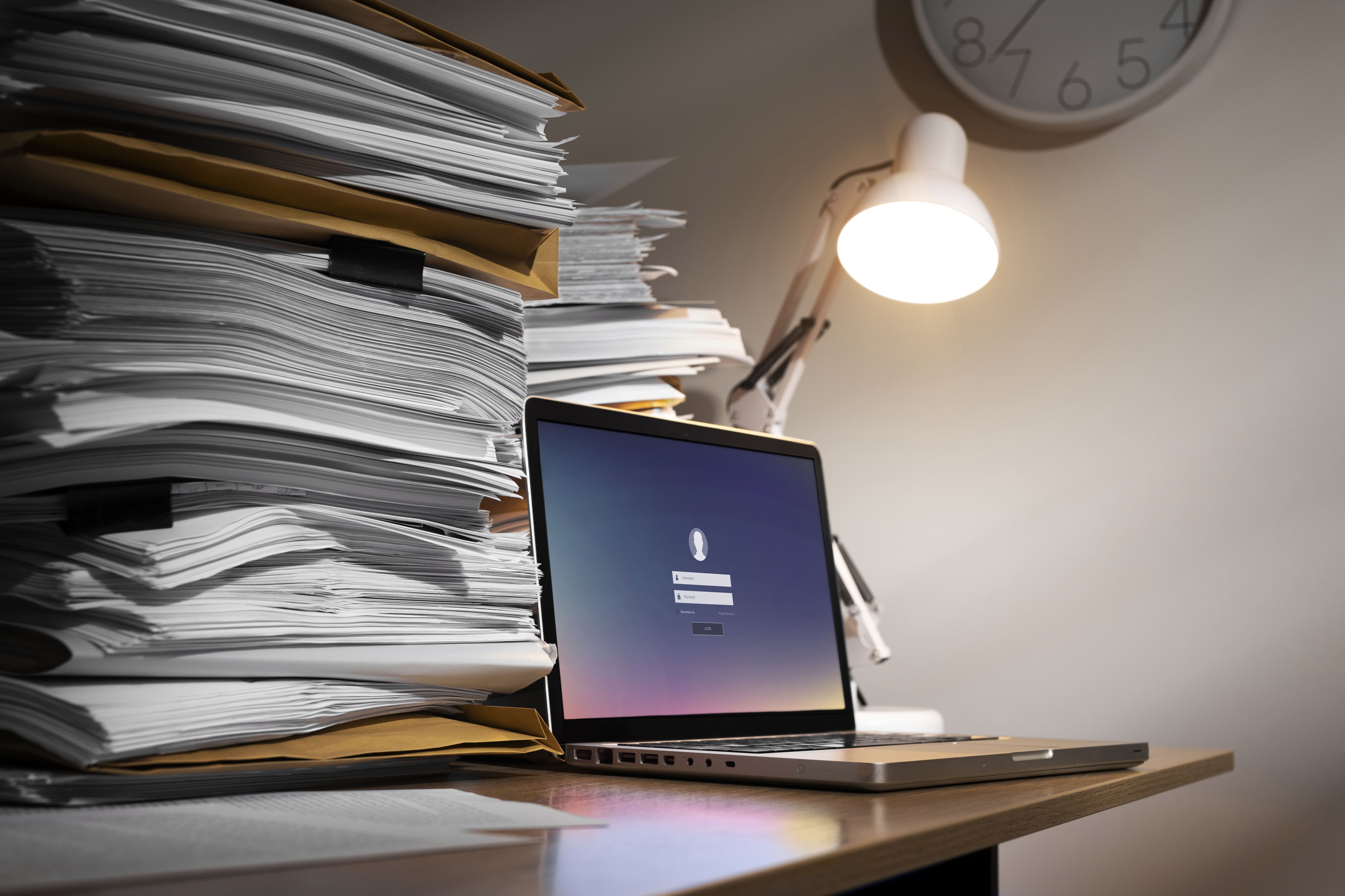 Contraste entre une pile imposante de dossiers papier et un ordinateur portable, symbolisant la transition vers la facturation électronique imposée par la Loi de Finances 2026 entreprise.