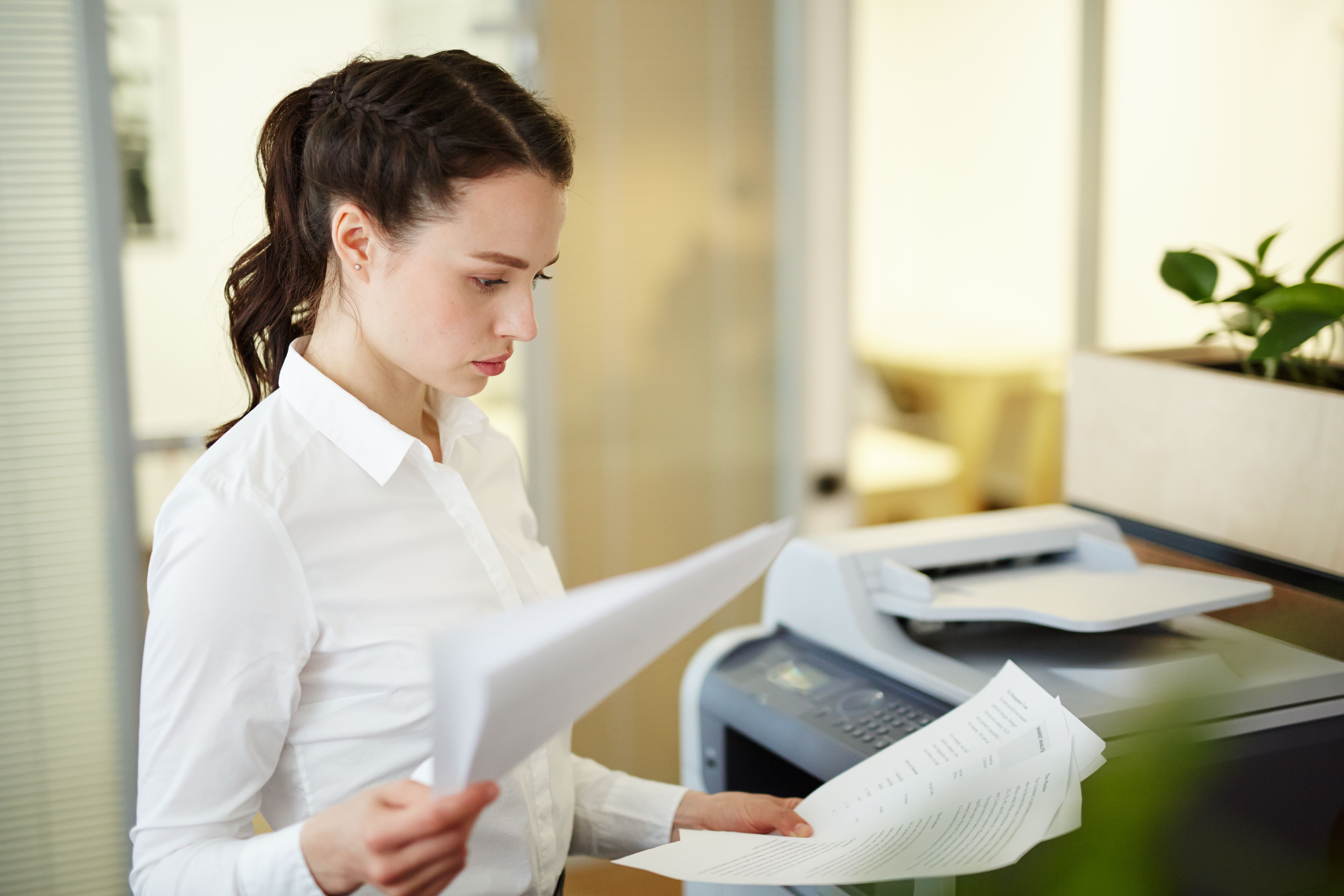 Une employée examine des documents imprimés avec une imprimante multifonction professionnelle 2026 dans un bureau.